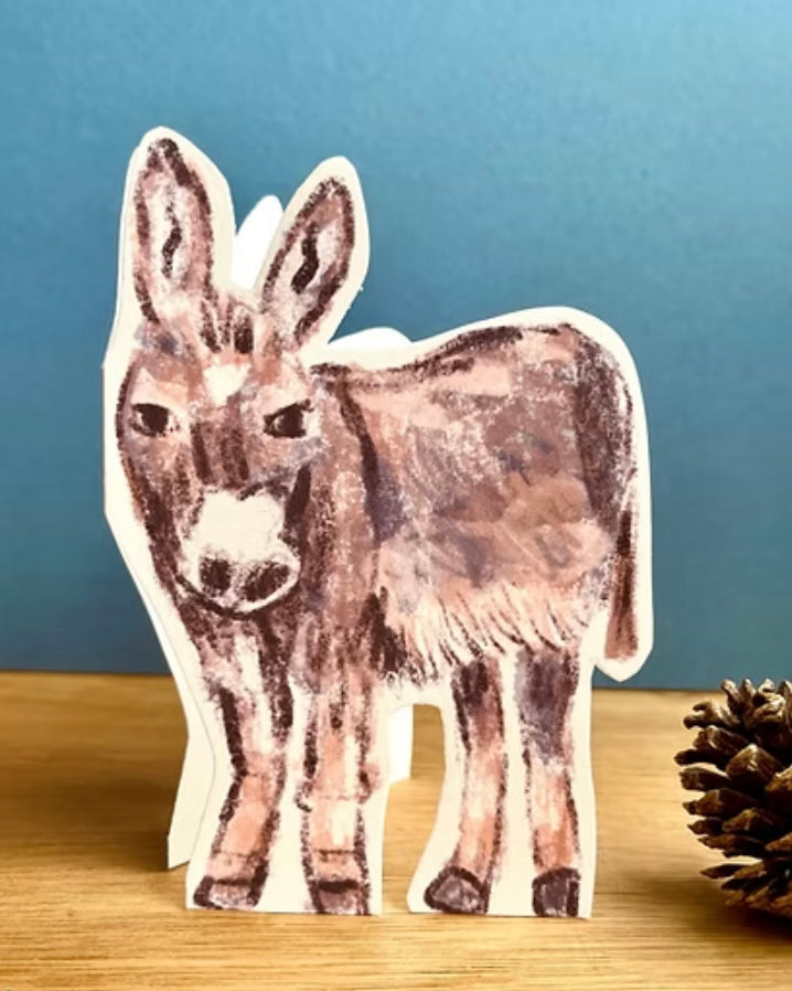 Donkey shaped Christmas card on a wooden surface with a blue background.