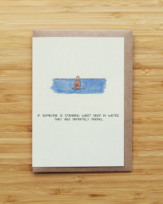 Card with a humorous illustration of a person standing in water and text, on a wooden surface.