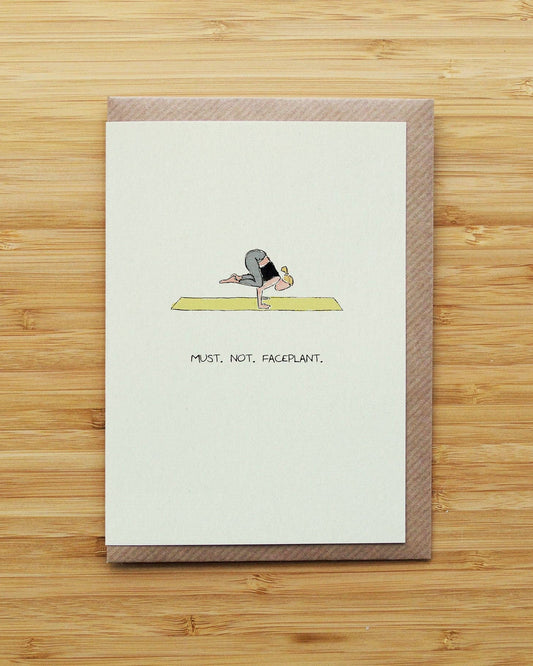 Card with a humorous illustration of a person falling face-first on a yoga mat, on a wooden surface.