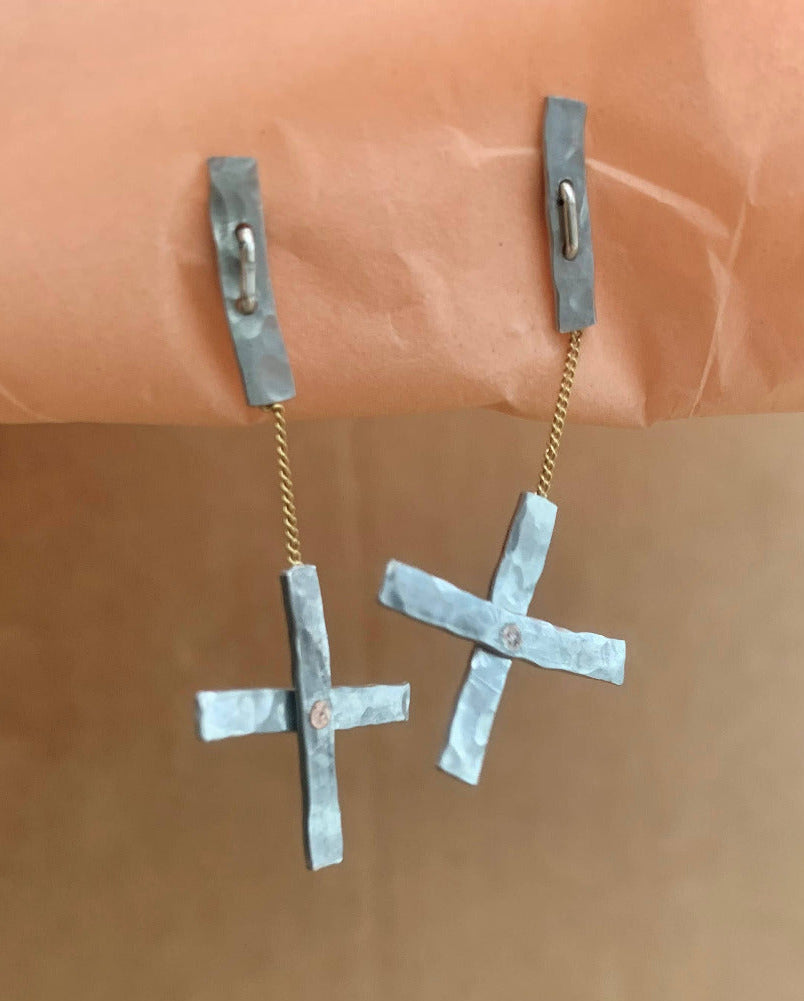 Pair of silver cross-shaped earrings on a brown background