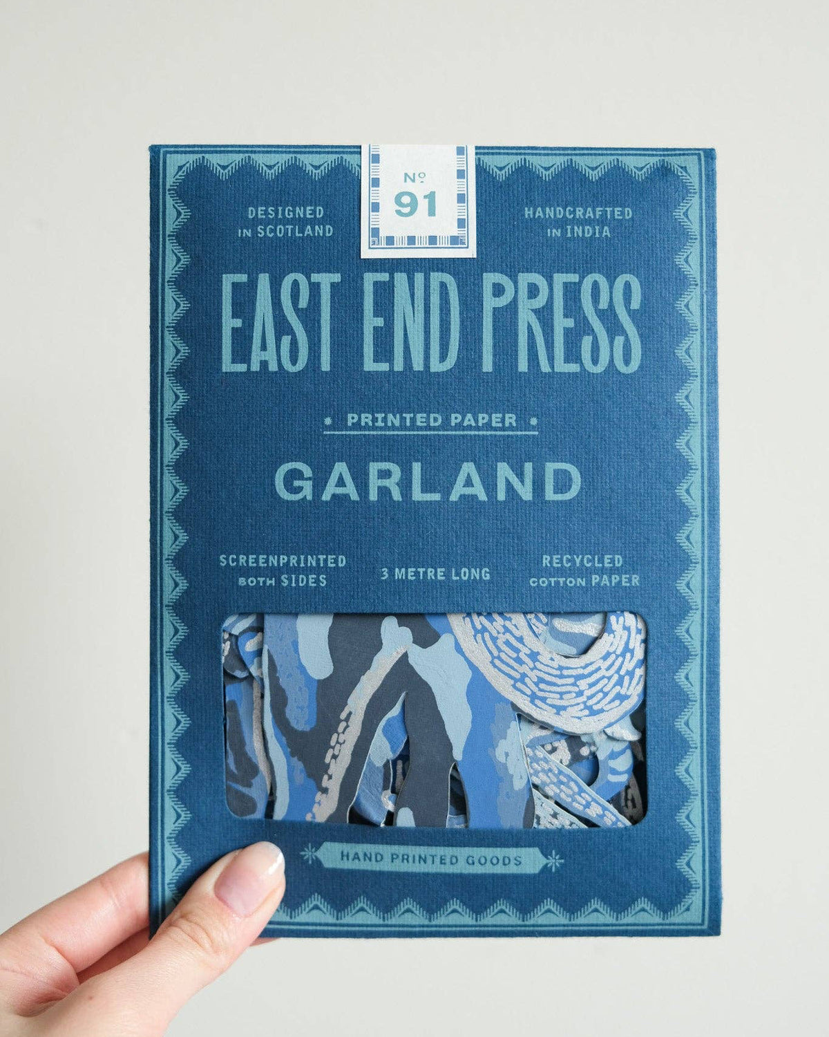 A hand holding East End Press Garland printed paper sheet No. 91 against a plain light gray background.