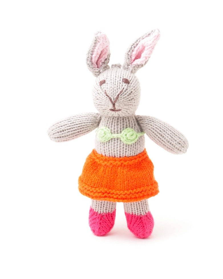 A knitted stuffed bunny doll with light gray yarn, pink inner ears, an orange skirt, and pink shoes, photographed against a plain white background.