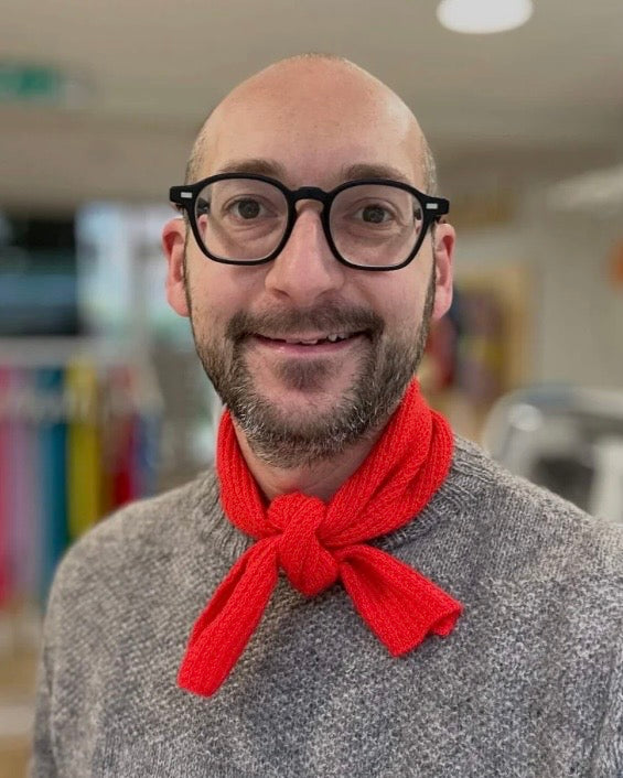 Man wearing a red neckerchief scarf and glasses in an indoor setting