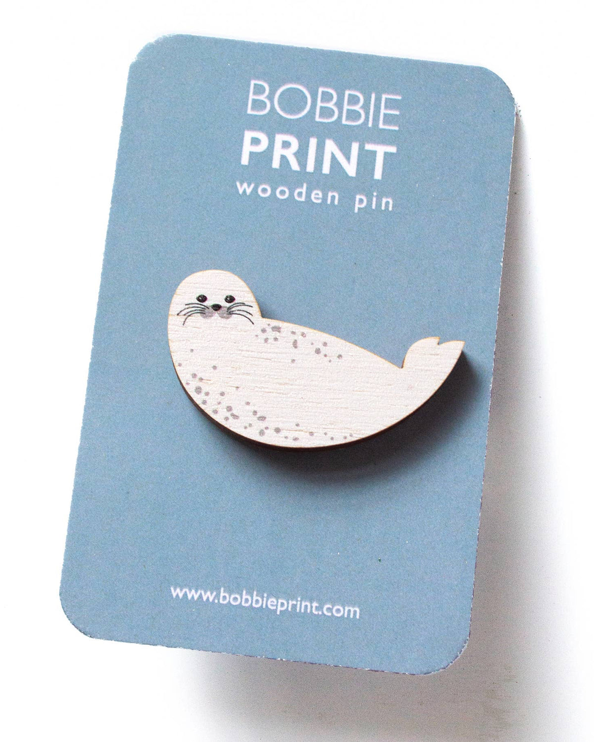 Wooden seal pin on a blue card with 'Bobbie Print' branding