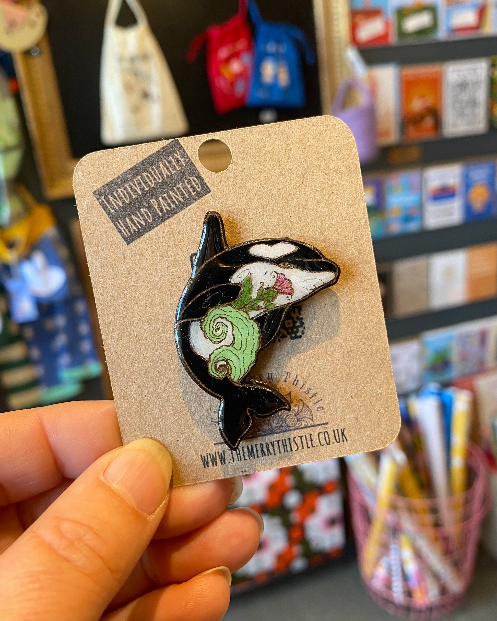 Orca whale pin on a card held by a hand with a store background