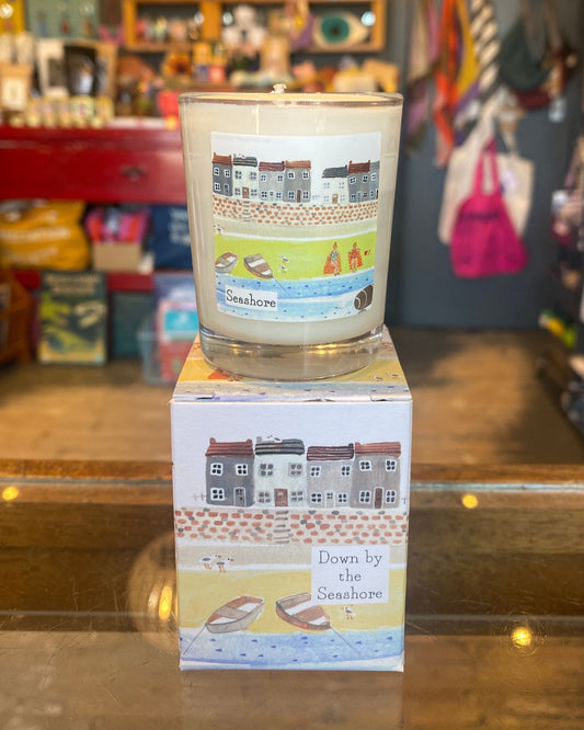 Votive candle on top of matching box with the word Seashore, in a store setting.
